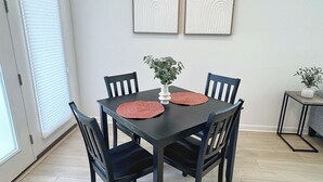 Un coin repas avec une table en bois foncé, quatre chaises, deux sets de table rouges, un vase blanc contenant une plante et deux œuvres d’art encadrées accrochées au mur.