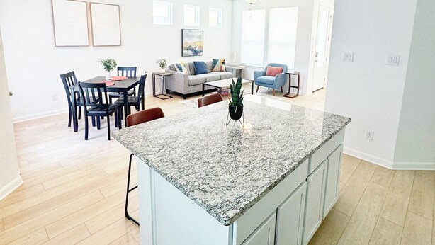 Une cuisine moderne dotée d’un îlot en granit, de meubles blancs et d’un coin repas avec une table et des chaises.