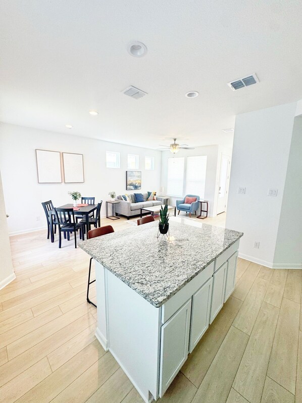 A modern kitchen with a granite island, white cabinetry, and a dining area with a table and chairs.