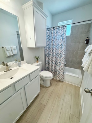 A modern bathroom with a white vanity, a toilet, a shower with patterned curtains, and a bathtub.