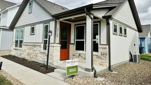 Une maison à deux étages, avec des fondations en pierre, un revêtement extérieur blanc et une porte rouge. Une pancarte indiquant « VENDU » est affichée devant.
