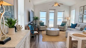A spacious living room with a large window, a ceiling fan, and a view of the ocean. - Gulf-Front Paradise 3BR Beach House Prime Location (Saint George Island)