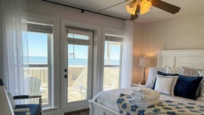 A bedroom with a bed, a chair, a nightstand, a lamp, and a view of the ocean through a door. - Gulf-Front Paradise 3BR Beach House Prime Location (Saint George Island)