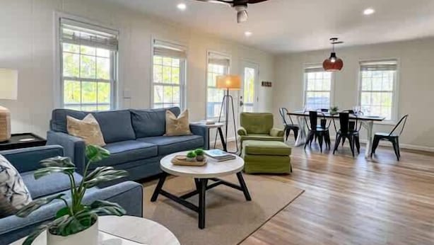 A spacious living room with a sofa, a coffee table, a dining table with chairs, and a ceiling fan.