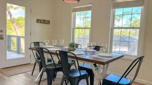 A dining area with a table set for four, surrounded by chairs, large windows, and a view of greenery.