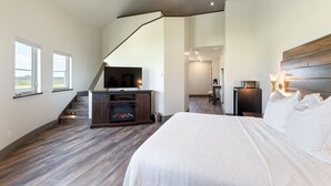 Een slaapkamer met een groot bed, een televisie, een open haard en een trap naar een andere kamer.