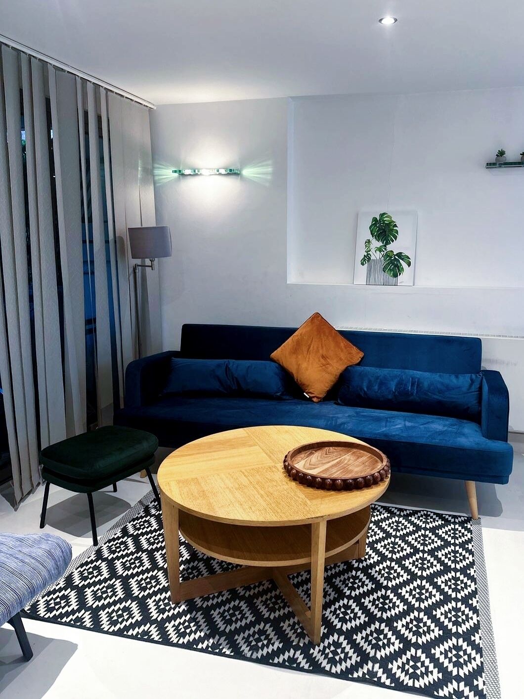 Een moderne woonkamer met een blauwe bank, een ronde houten salontafel en een zwart-wit tapijt.