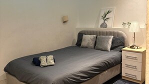 A modern bedroom with a large bed, a bedside table, a lamp, and a wall-mounted shelf with plants. - Modern 1bed sleeps 4 @London Bridge (London)