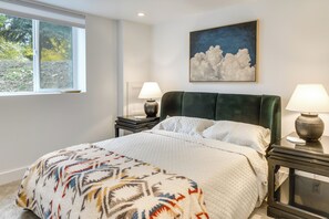 A bedroom with a bed, two bedside tables with lamps, a window with a view of trees, and a painting of clouds on the wall. - Mountain-View Home Near Hiking in Alpine! (Alpine)