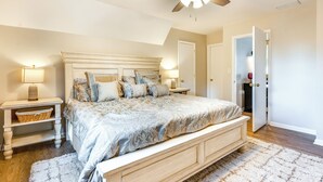 A bedroom with a large bed, wooden headboard, two bedside tables with lamps, a ceiling fan, and a door leading to another room. - Dock & Hot Tub at High Rock Lake Retreat (Lexington)