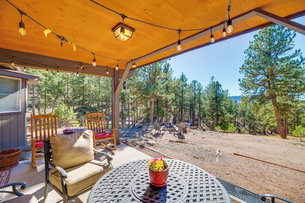 A covered outdoor seating area with chairs and a table, overlooking a forested landscape. - Fish, Hike & Sightsee: Lovely Florissant Cabin! (Florissant)