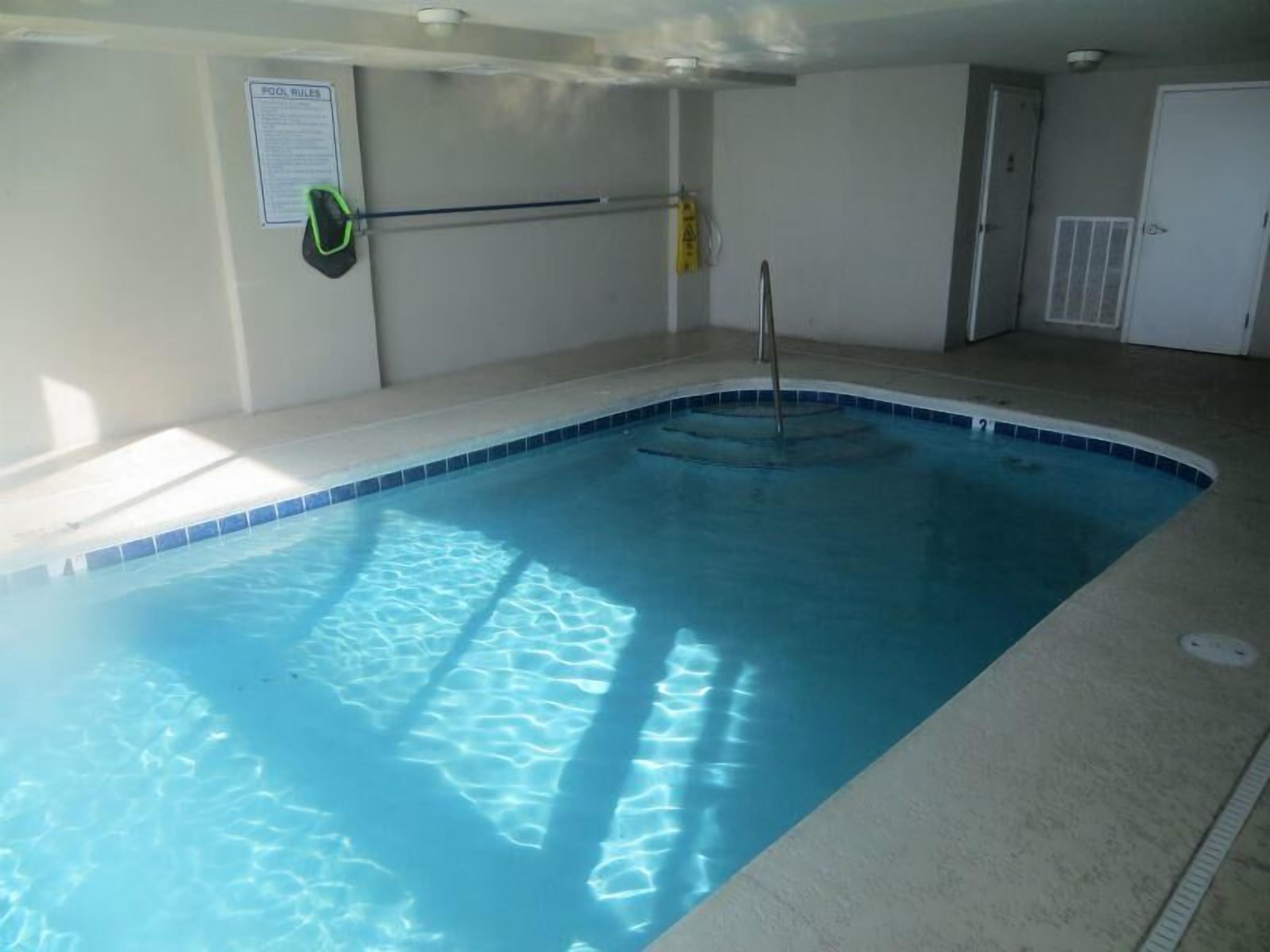 An indoor swimming pool with a tiled edge, a pool ladder, and a safety sign on the wall.