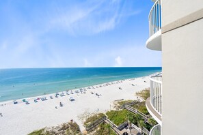 A beach with a clear sky, a white building with a balcony, and a wooden walkway leading to the beach. - Tradewinds 903 (Orange Beach)