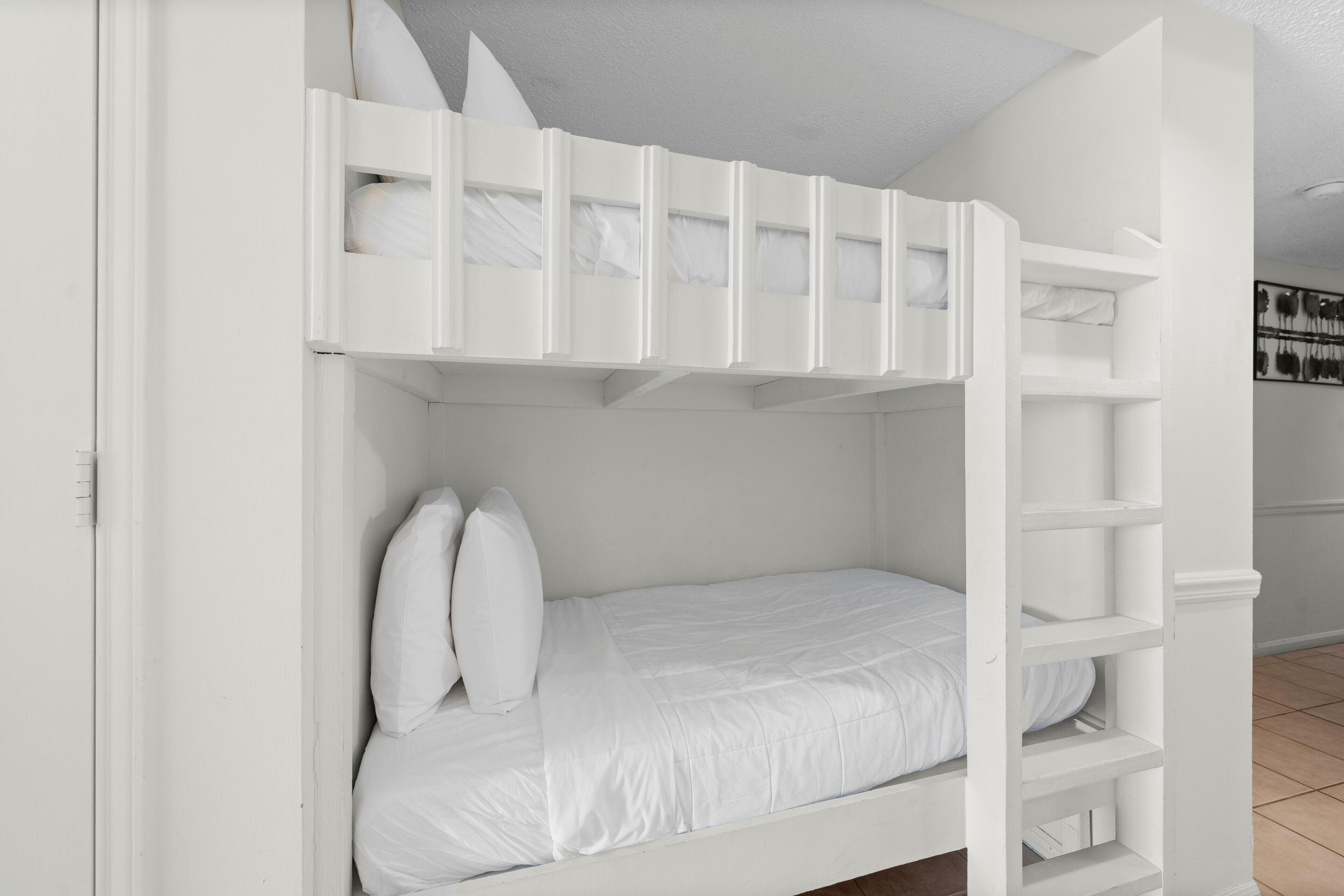 Ein Etagenbett mit weißer Bettwäsche und Kissen, ein weißer Kleiderschrank und ein gefliester Boden.