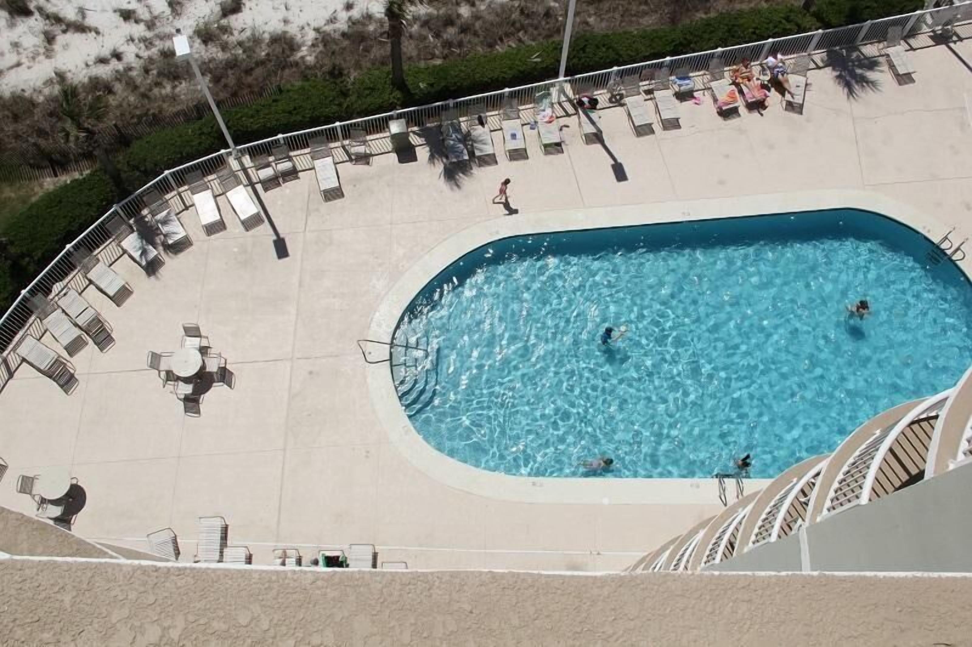 Vista aérea de una piscina con sillas de descanso y zona sombreada.