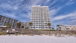 Ein Hochhaus-Hotel mit mehreren Balkonen, nahe eines Strandes mit Holzstegen.