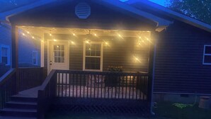 Una casa de madera con un porche, luces de cuerda y una pequeña mesa con sillas.