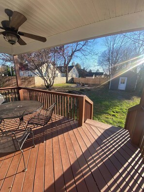 A wooden deck with a table and chairs, a ceiling fan, and a view of a backyard with a house and trees.