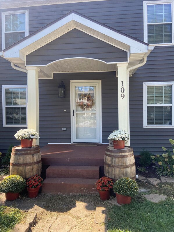 A two-story house with a front porch, a number '109' on the door, and potted plants on either side of the entrance.