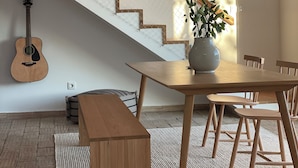 Ein modernes Interieur mit einer Holztreppe, einem Esstisch mit Stühlen, einer Bank, einer Gitarre und einer Pflanzvase.