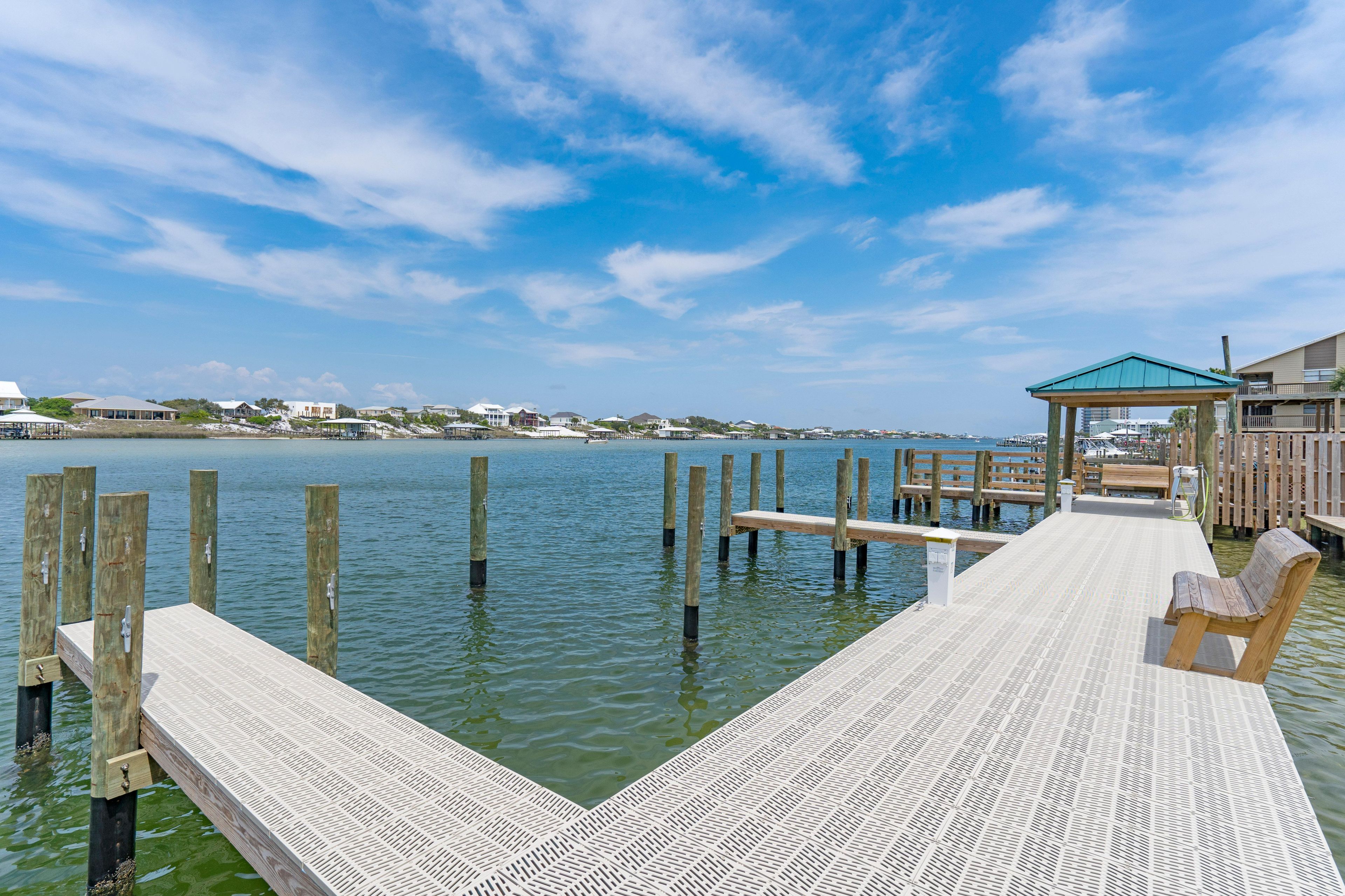 A wooden pier extending into calm water with a wooden bench and a gazebo.