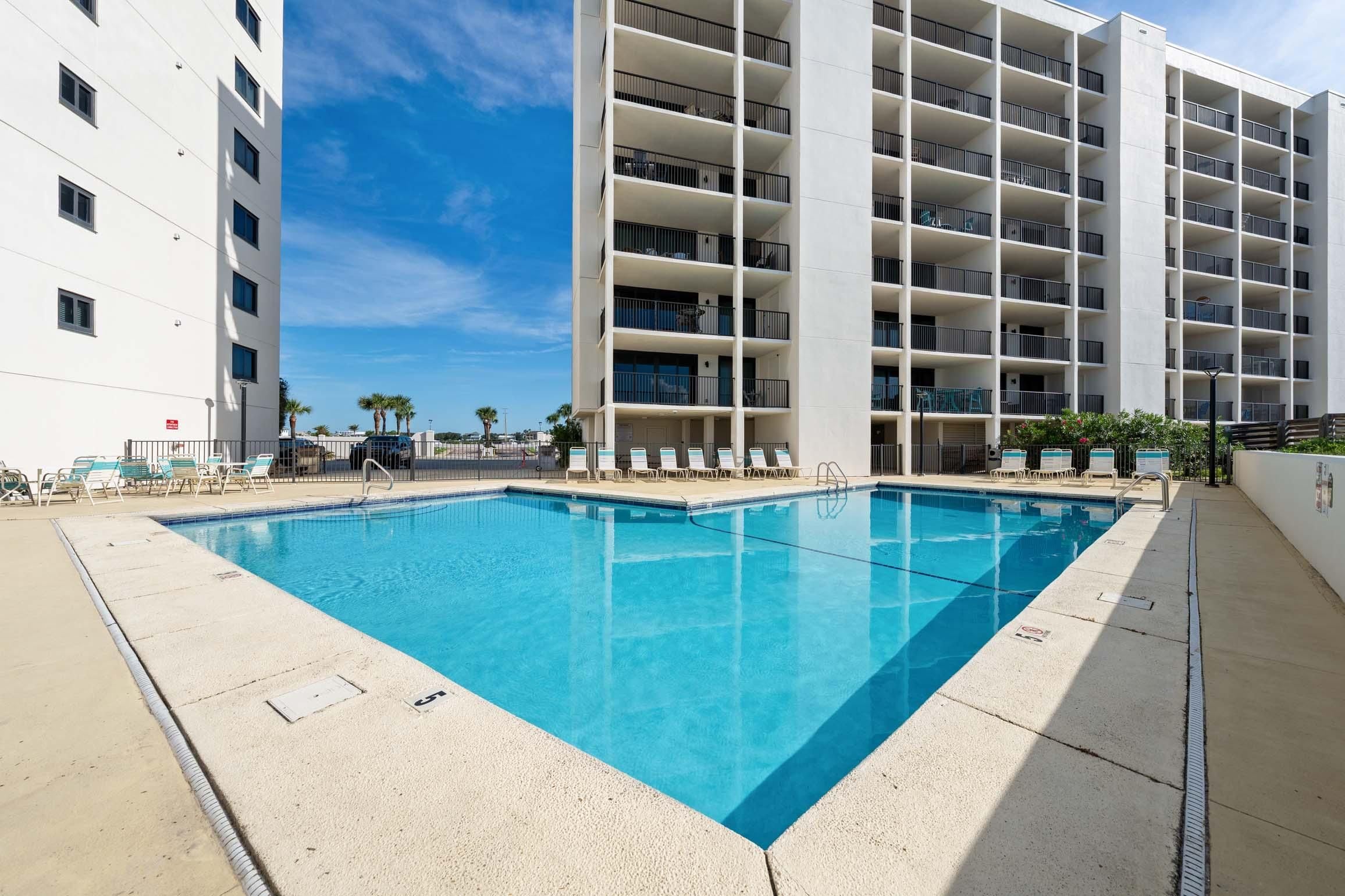 A swimming pool with lounge chairs and a multi-story building with balconies.