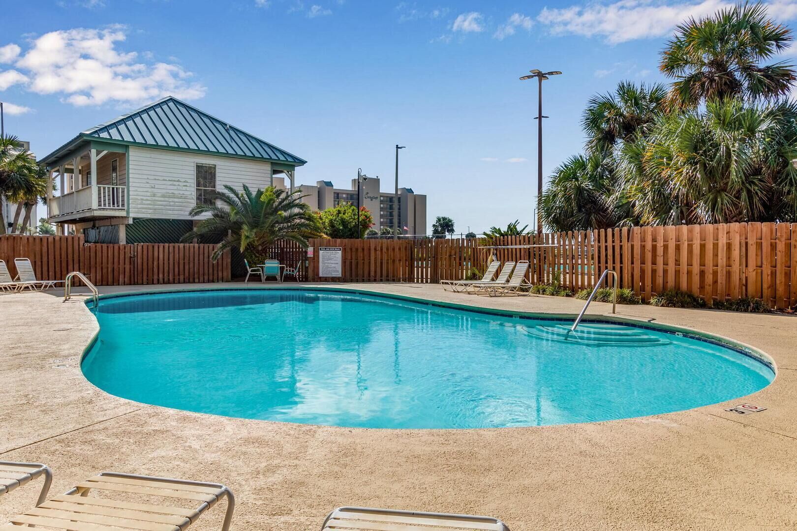 A swimming pool with lounge chairs and a wooden fence.