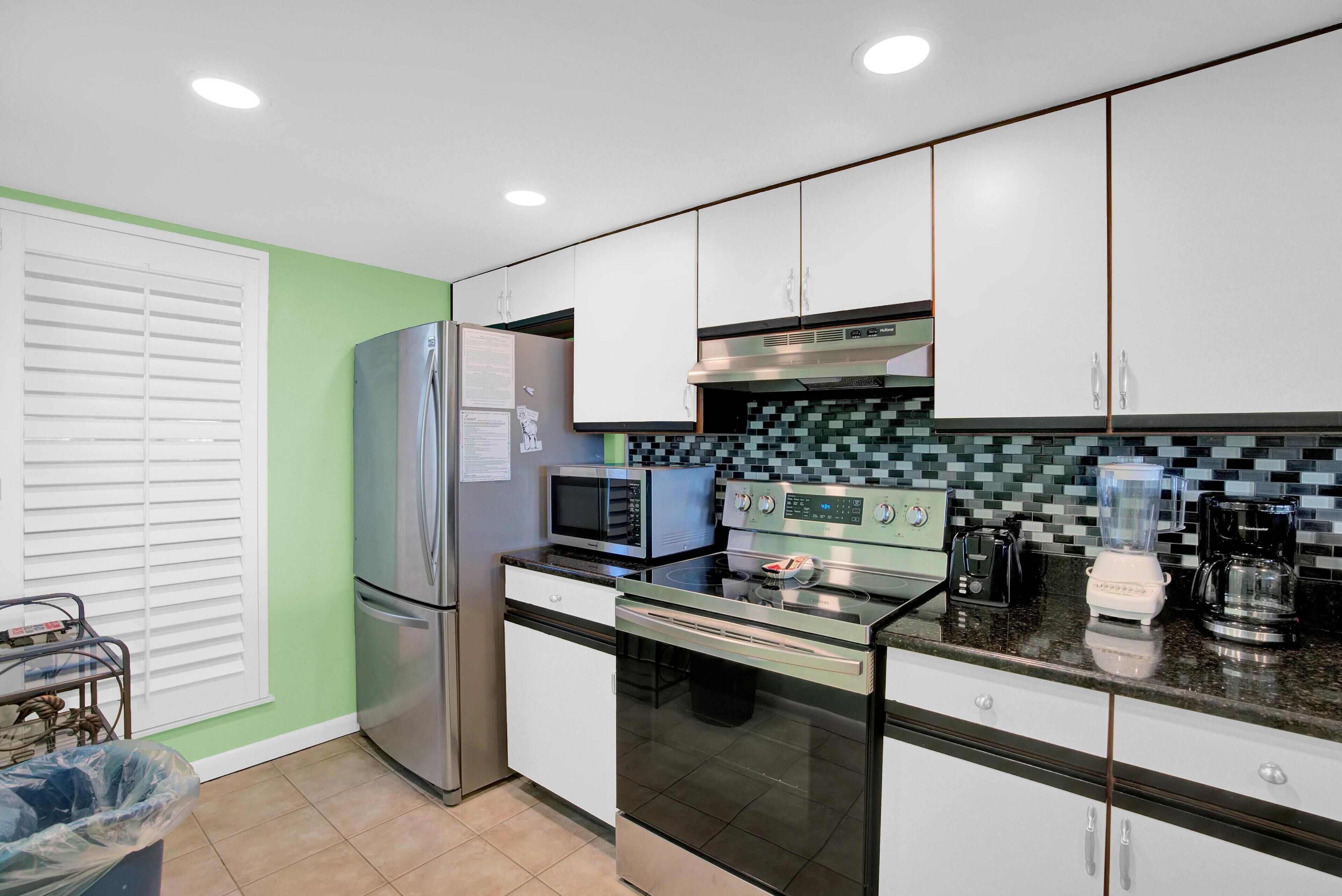 A modern kitchen with stainless steel appliances, white cabinets, and a tiled backsplash.