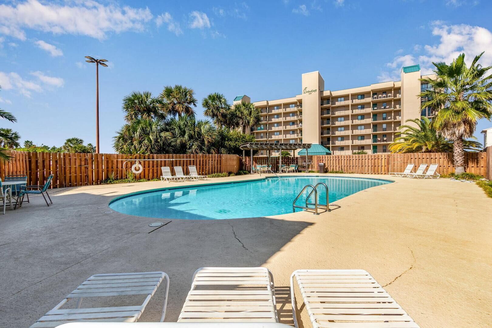 A hotel with a swimming pool, lounge chairs, and a wooden fence.