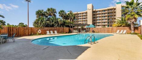 A hotel with a swimming pool, lounge chairs, and a wooden fence.