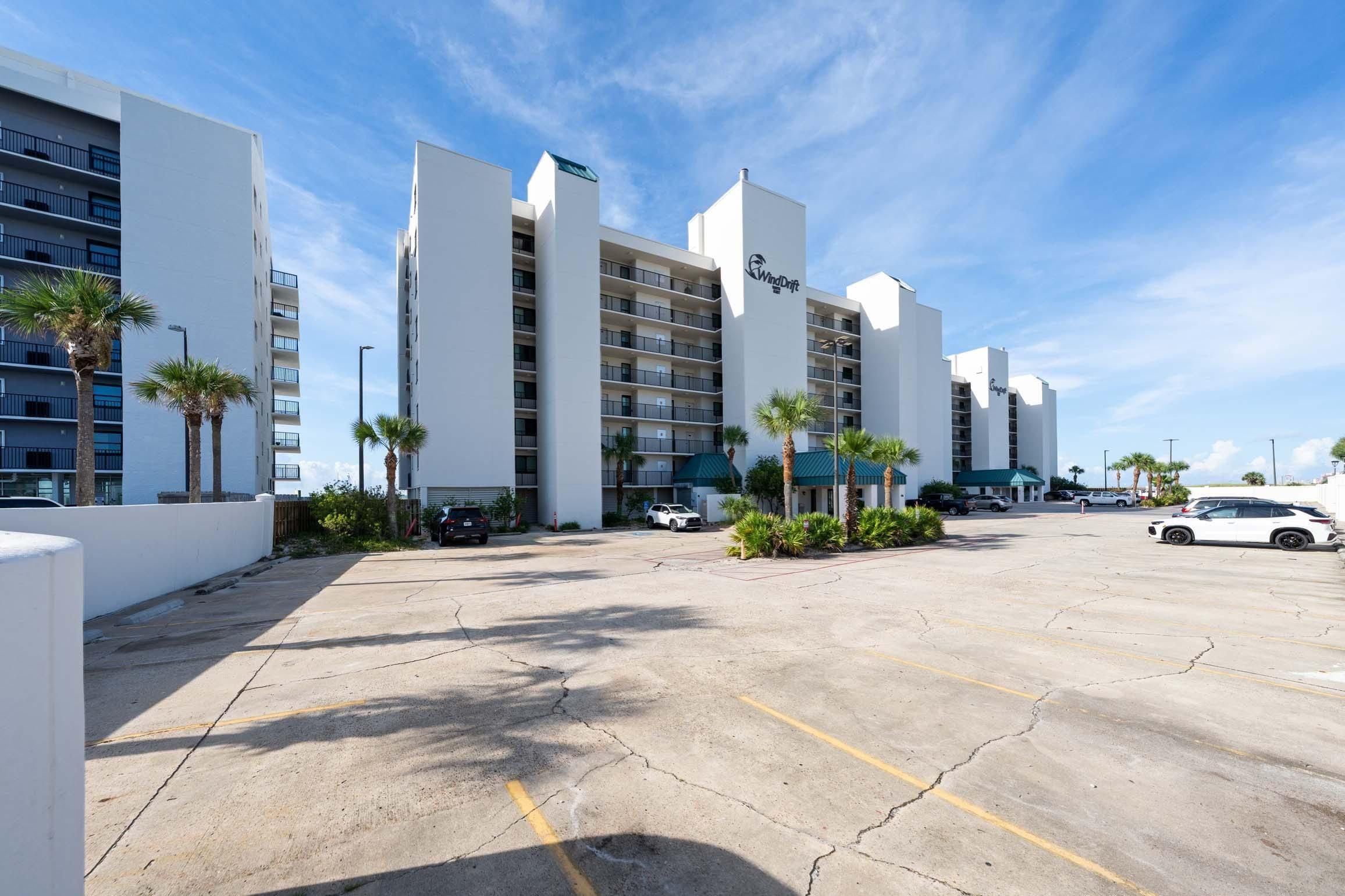 A multi-story hotel with a parking lot, palm trees, and a clear sky.