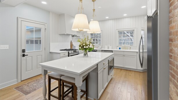 Una cocina moderna con armarios blancos, una isla central, iluminación colgante y un refrigerador de acero inoxidable.