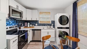 A compact kitchen with white cabinets, a microwave, a dishwasher, and a built-in oven. There is a window with blinds and a potted plant on the counter. - Vibey 2-bedroom unit in duplex in Nashville (Madison)