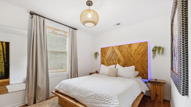 A modern bedroom with a wooden headboard, a large window with curtains, a bedside table, and a hanging light fixture. - Vibey 2-bedroom unit in duplex in Nashville (Madison)