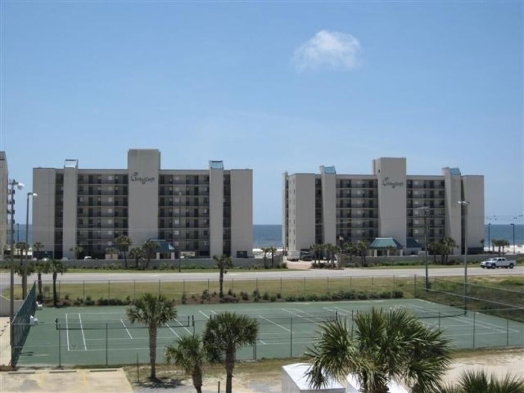Blick auf ein Hotel mit Tennisplatz im Vordergrund und Strand in der Ferne.