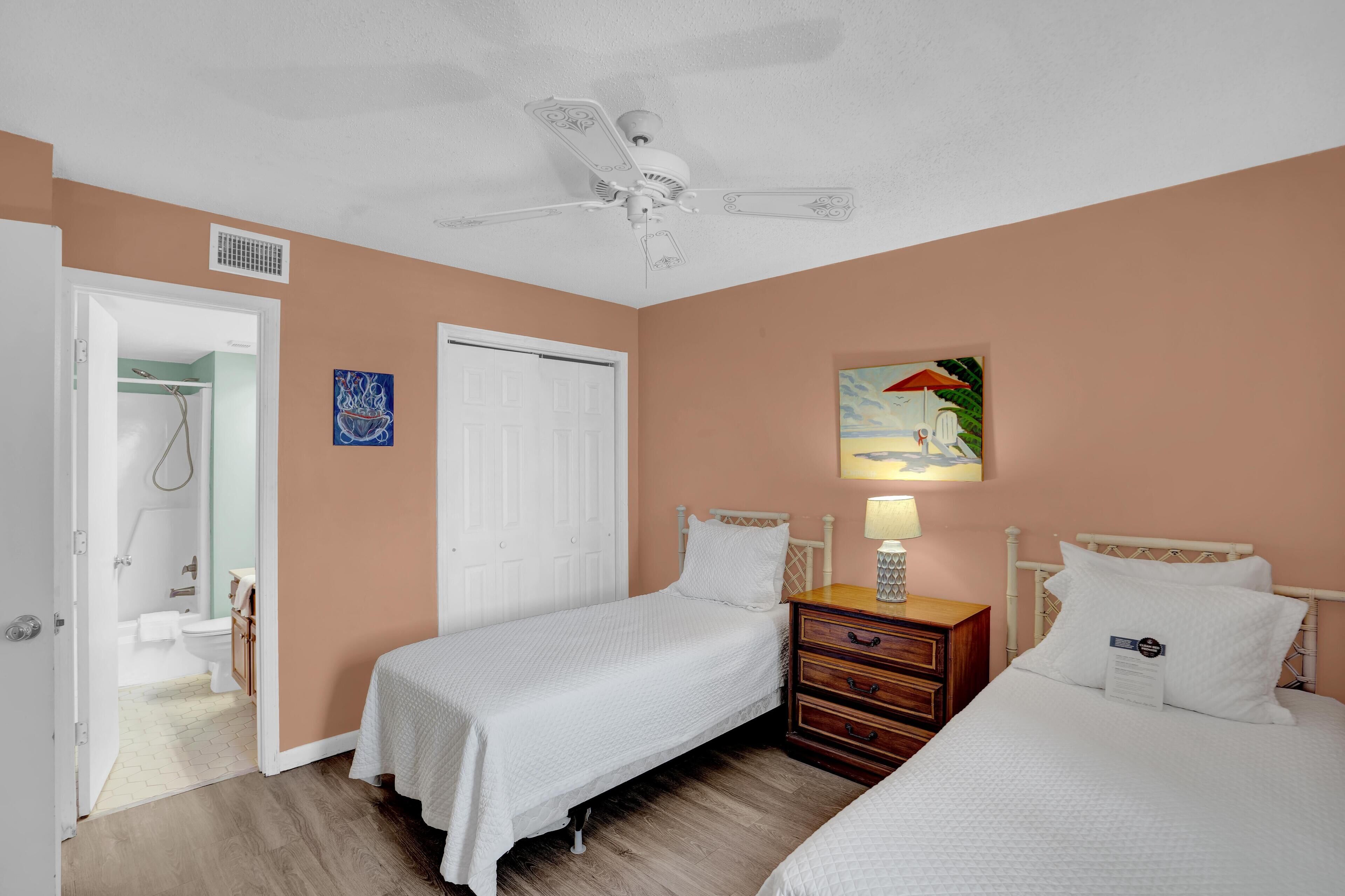 A bedroom with two beds, a ceiling fan, a nightstand, and a painting on the wall.