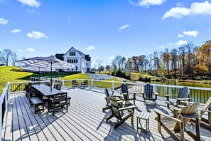 Eine Holzterrasse mit Adirondack-Stühlen, einem Tisch und einem weißen Zaun.