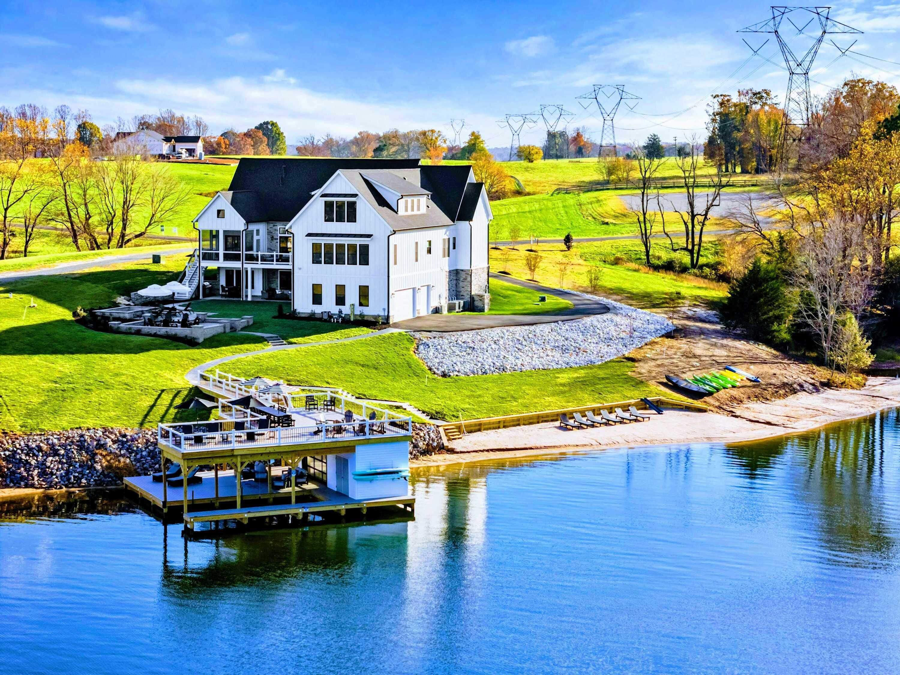 Une grande maison blanche avec un quai et un bateau, entourée d’un paysage verdoyant et bordée par une étendue d’eau.