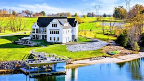 A large white house with a dock and a boat, surrounded by a green landscape and a body of water. - Lakefront Lake Anna, Pool, Beach, Dock (Mineral)