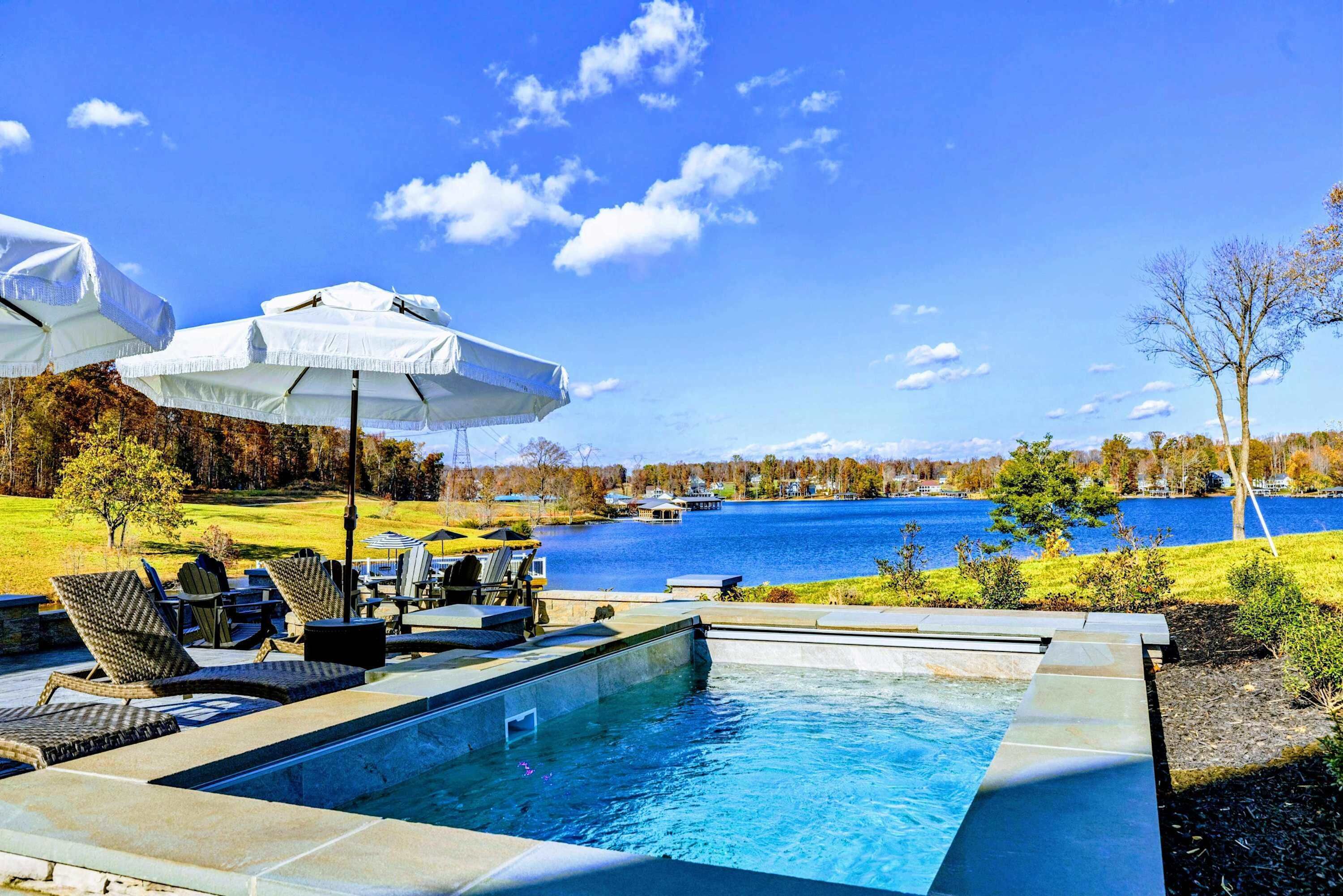Une piscine entourée d’un lac et d’arbres, avec des chaises longues et des parasols.