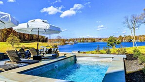 A swimming pool with lounge chairs and umbrellas, surrounded by a lake and trees. - Lakefront Lake Anna, Pool, Beach, Dock (Mineral)