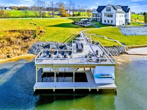 A waterfront property with a dock, outdoor seating area, and a large house in the background.