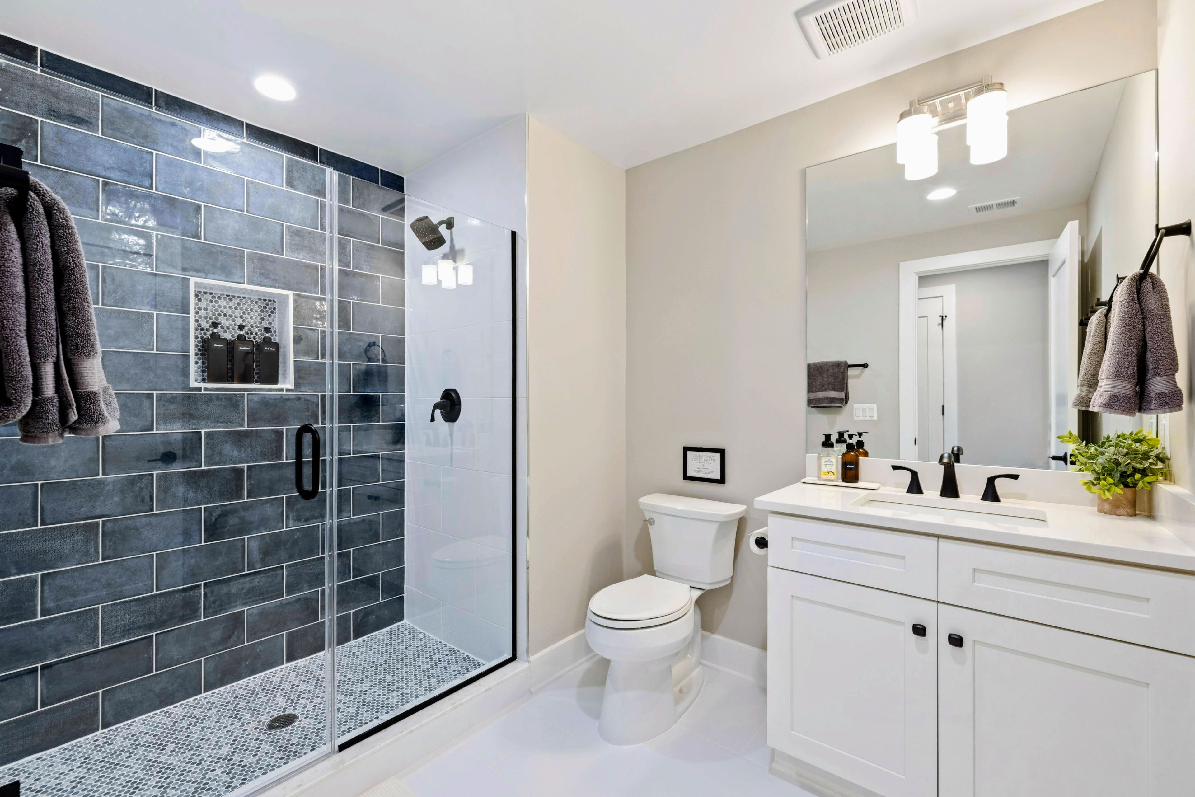 Une salle de bain moderne avec une douche à parois de verre, des toilettes blanches et un meuble-lavabo doté d’un grand miroir.