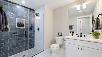 Une salle de bain moderne avec une douche à parois de verre, des toilettes blanches et un meuble-lavabo doté d’un grand miroir.