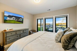 A bedroom with a large bed, a dresser, a chair, and a television displaying a house.