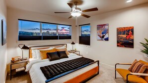 A modern bedroom with a large bed, a ceiling fan, and multiple windows offering views of the landscape. - Old Town Group Retreat - New to Brewery District! (Fort Collins)