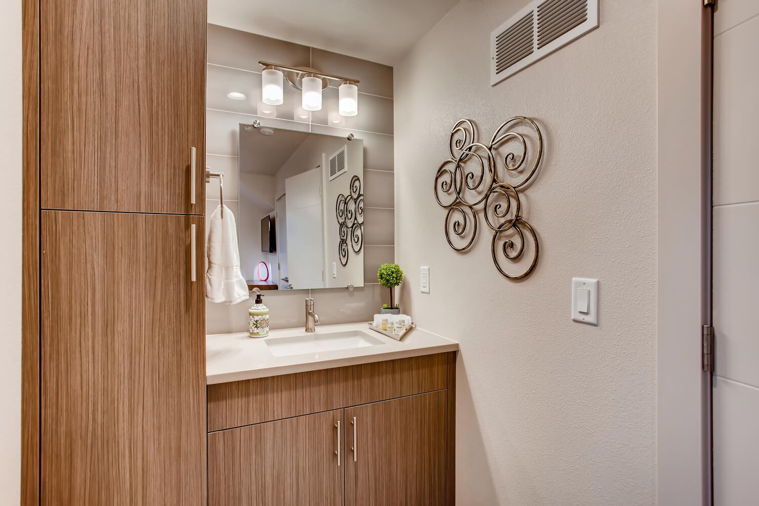 Une salle de bain moderne avec un meuble-lavabo en bois, un grand miroir et des œuvres d’art décoratives au mur.