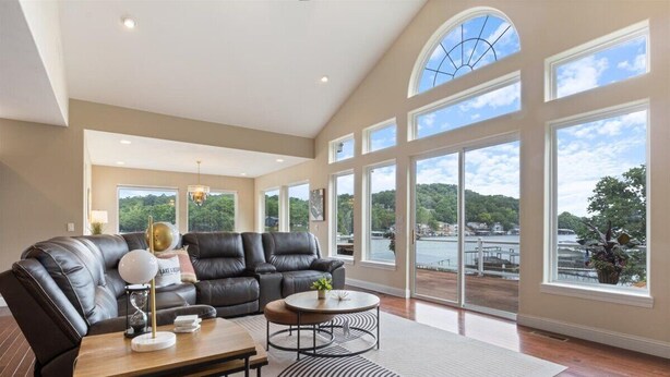 Ein geräumiges Wohnzimmer mit einer großen schwarzen Ledersofa, einem Couchtisch und Blick auf einen See durch große Fenster.