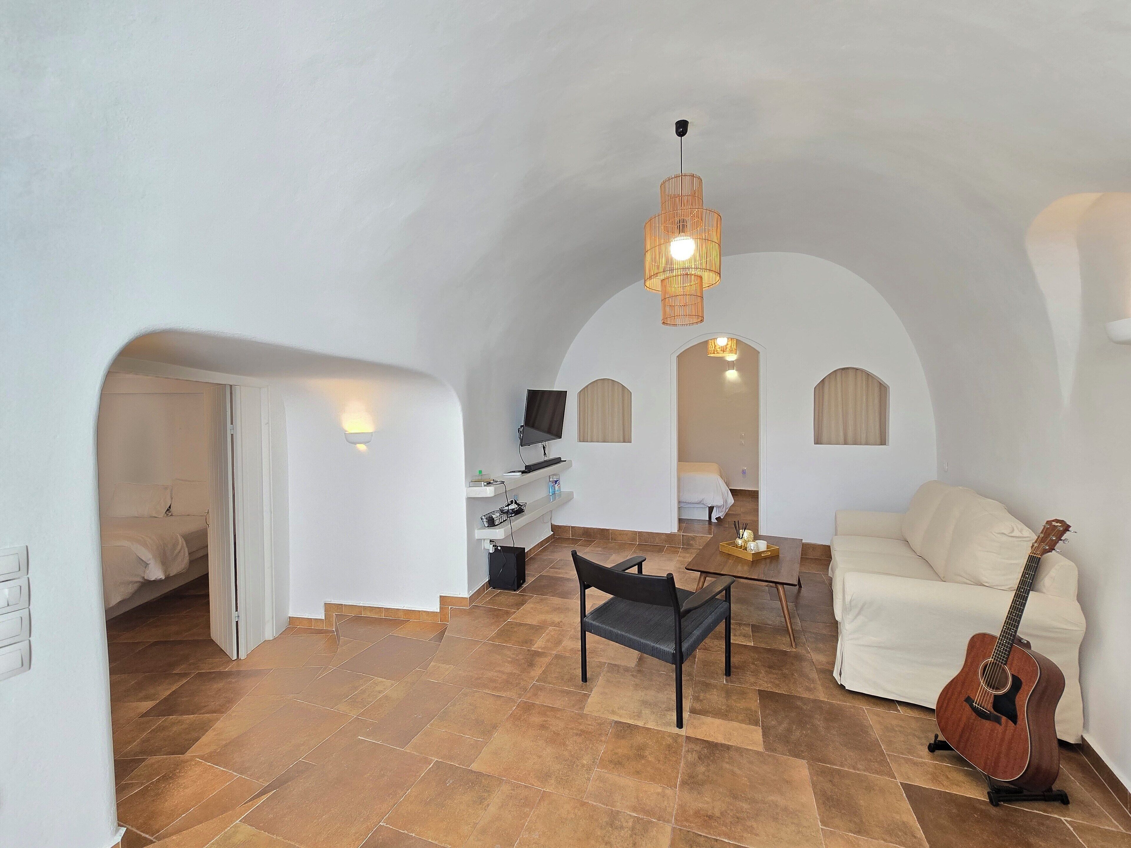 A spacious living area with a high ceiling, a sofa, a coffee table, a guitar, and a television.