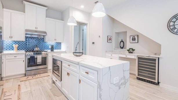 A modern kitchen with white cabinetry, a marble island, and a blue-tiled backsplash. - Charming 3-Bedroom Luxury Home 5Min -> Downtown, NRG and Medical Center. (Houston)